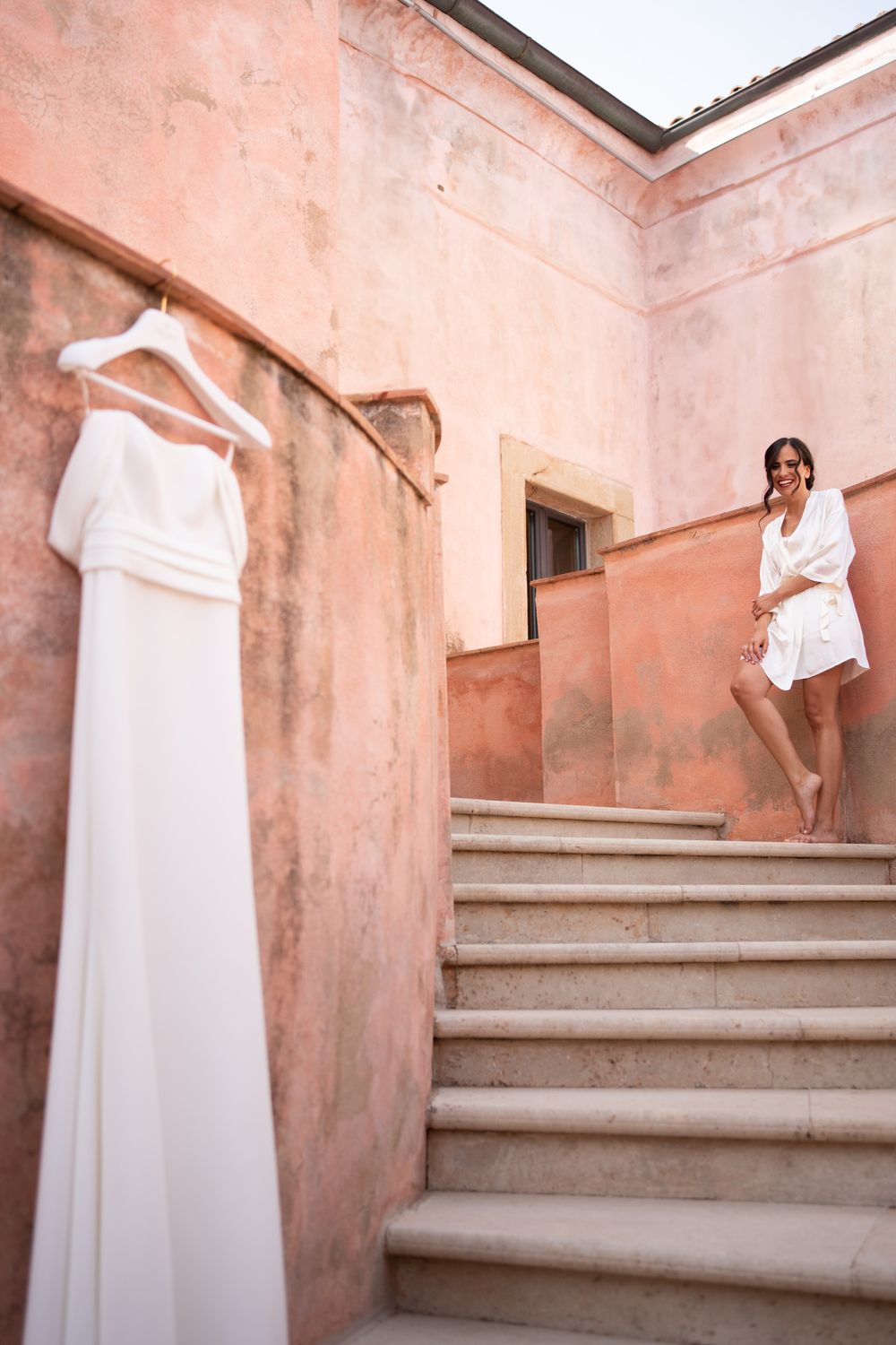 A white wedding dress hangs elegantly on display along pink-tinted stone stairs.