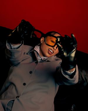 Stylish figure in grey coat and sunglasses striking dynamic poses in a red studio setting.