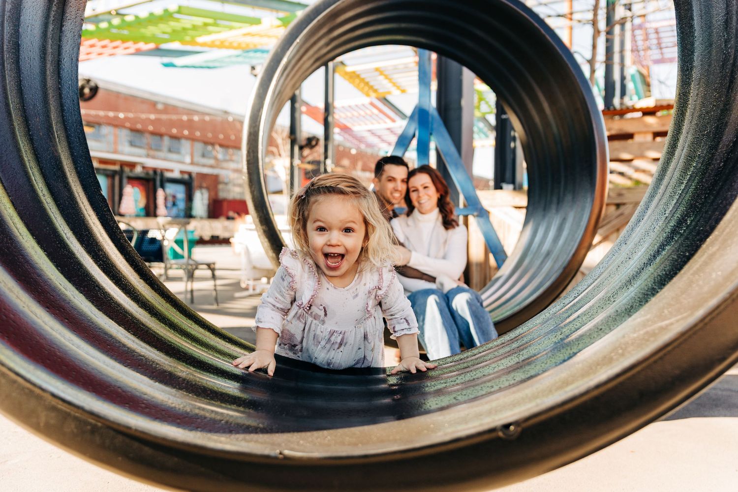 A little girl is excited while posing for photos with her family and looking through a giant circle swing in Camp North End.