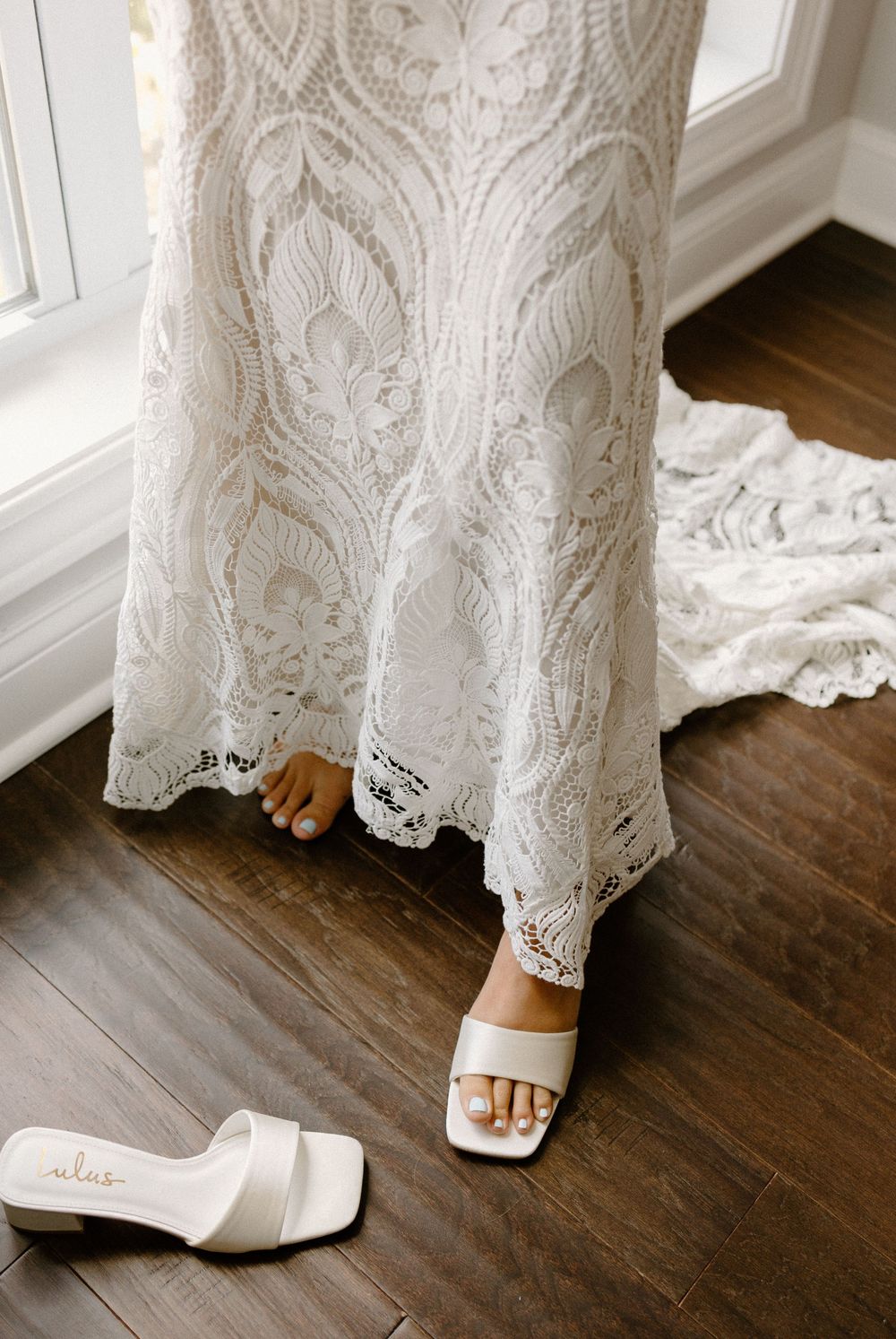 Close-up sequence of a detailed lace wedding dress hem and white shoes on hardwood flooring.