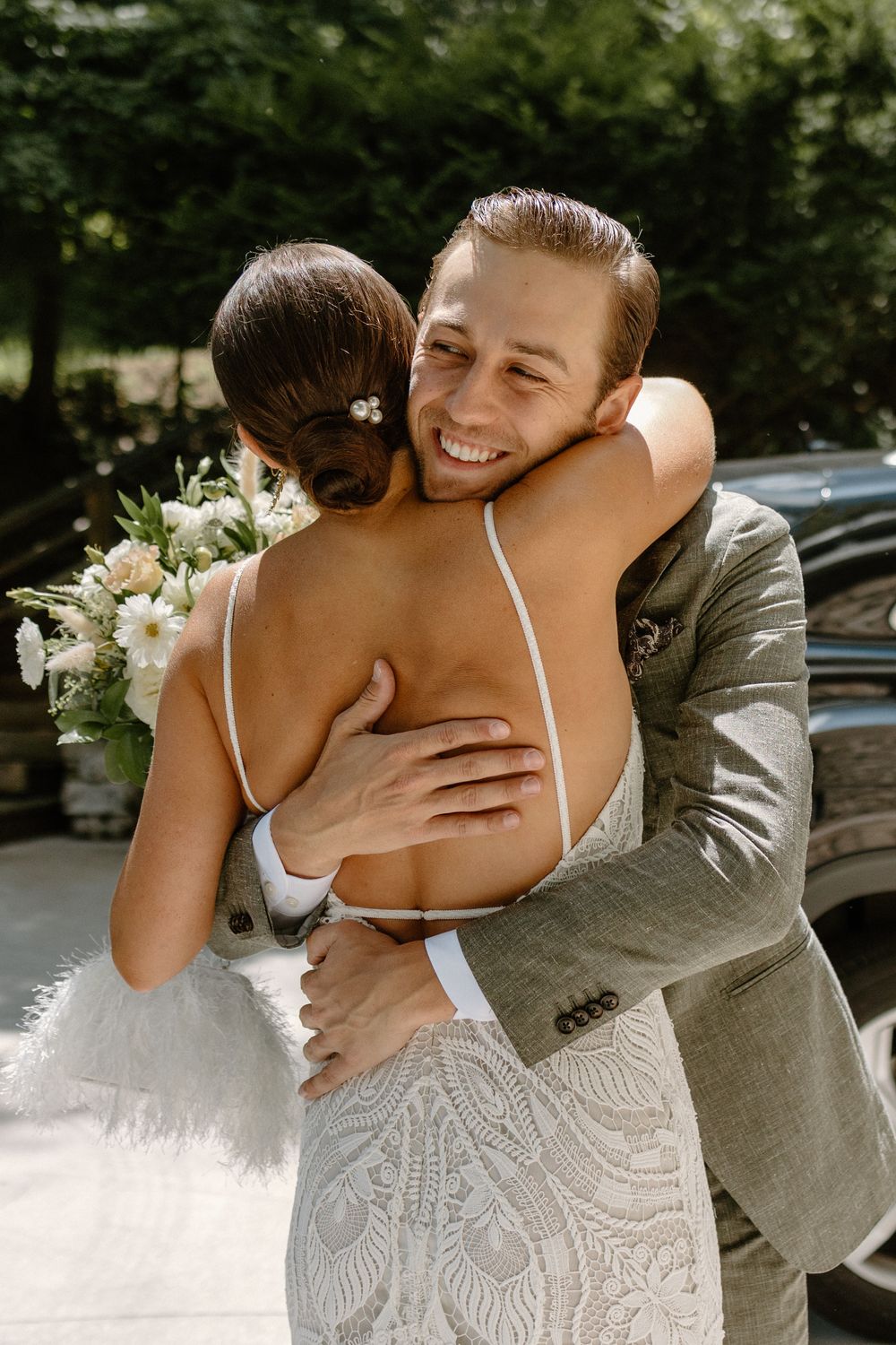 Couple sharing an intimate embrace outdoors with white floral bouquet.