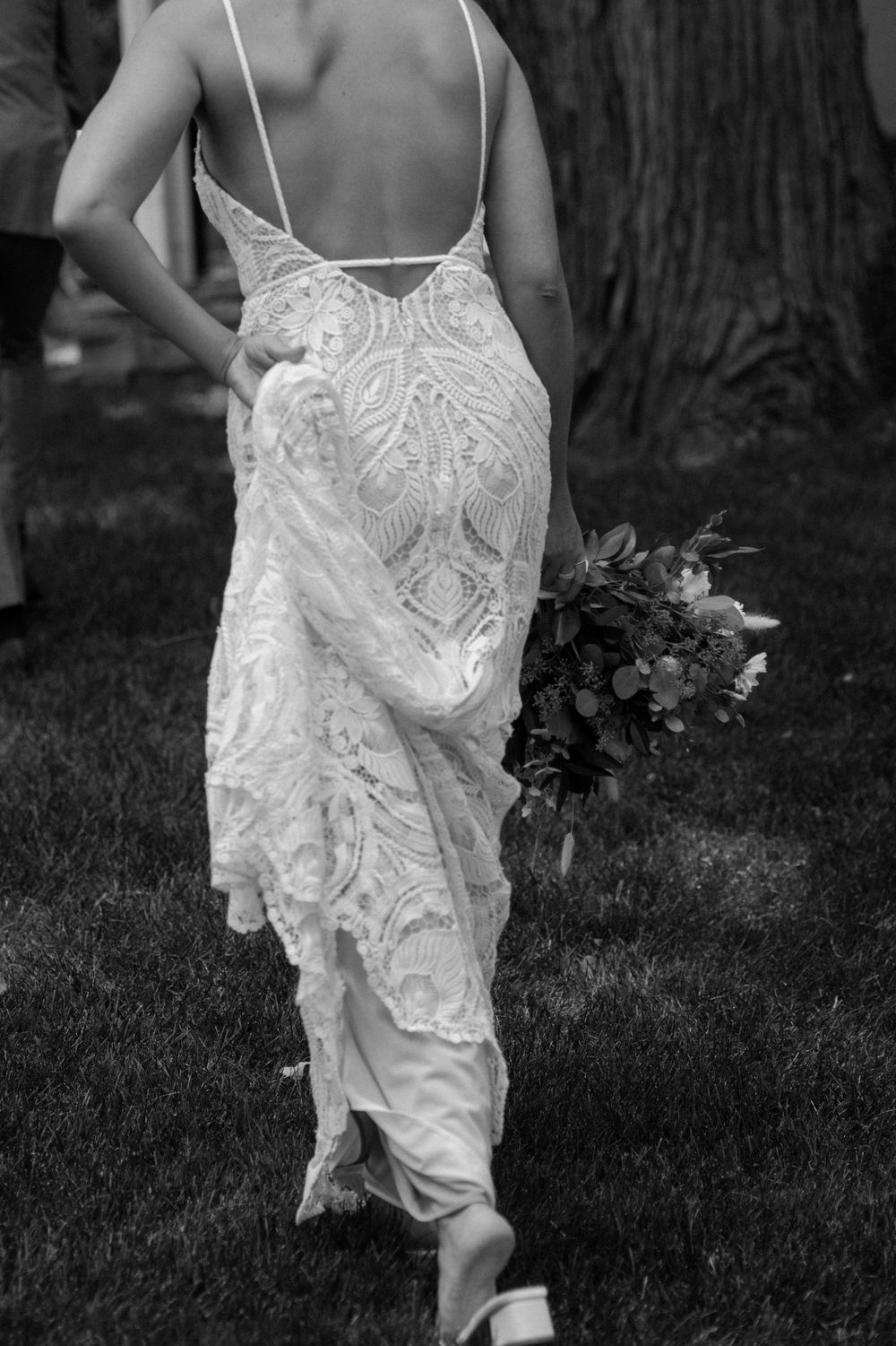 Back view of a detailed lace wedding dress as the wearer walks through a garden setting.