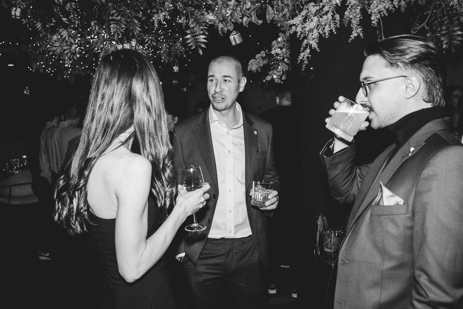 Three guests socializing with wine glasses at upscale evening party in black and white photo.