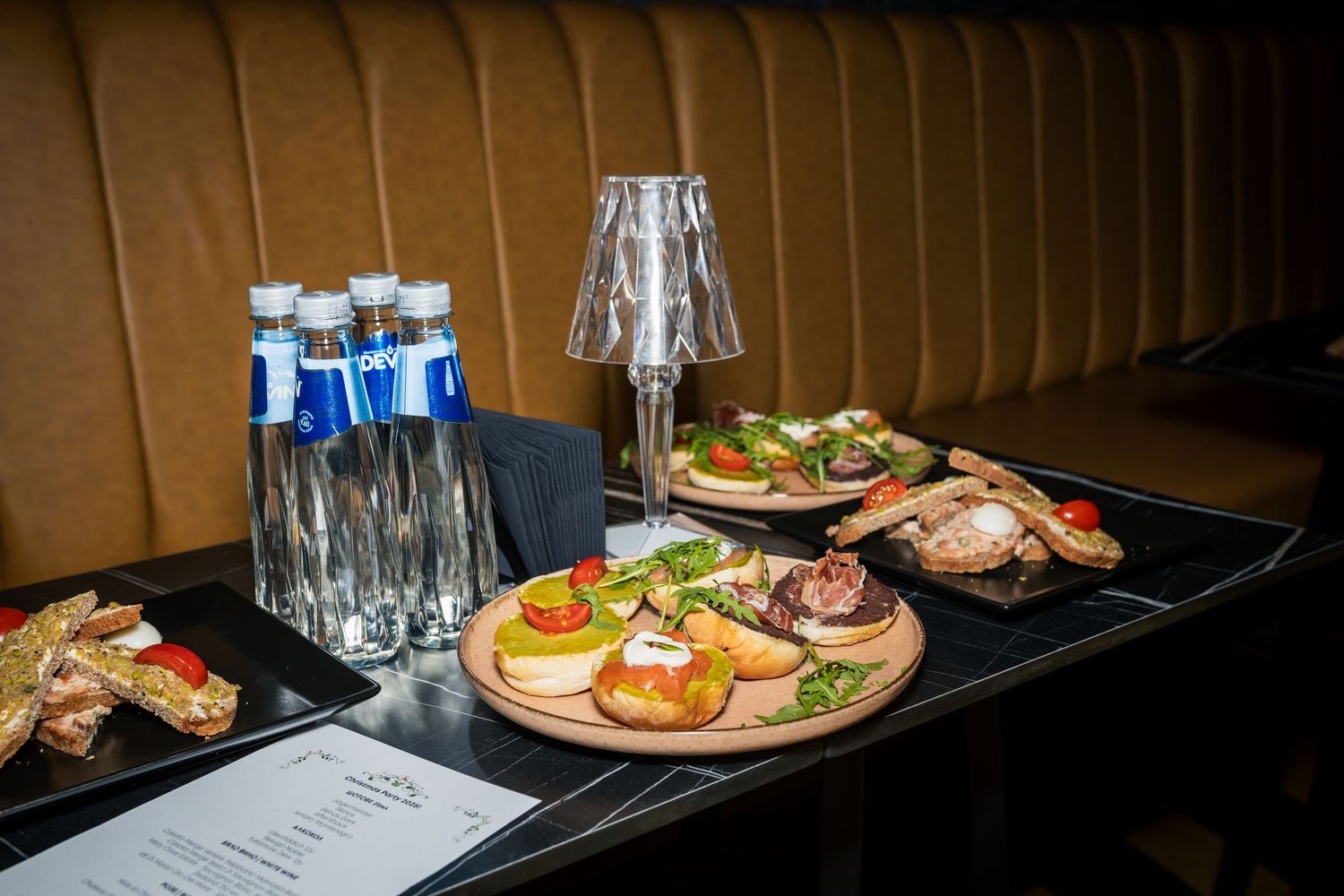 Elegant party food spread with canapes, water bottles and appetizers on dark restaurant table.