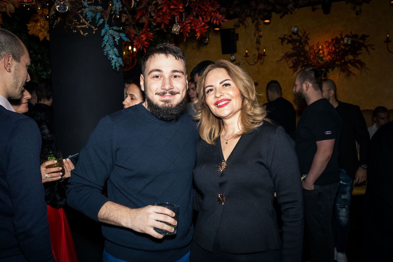 Bearded man and blonde woman smiling together at indoor social gathering event.