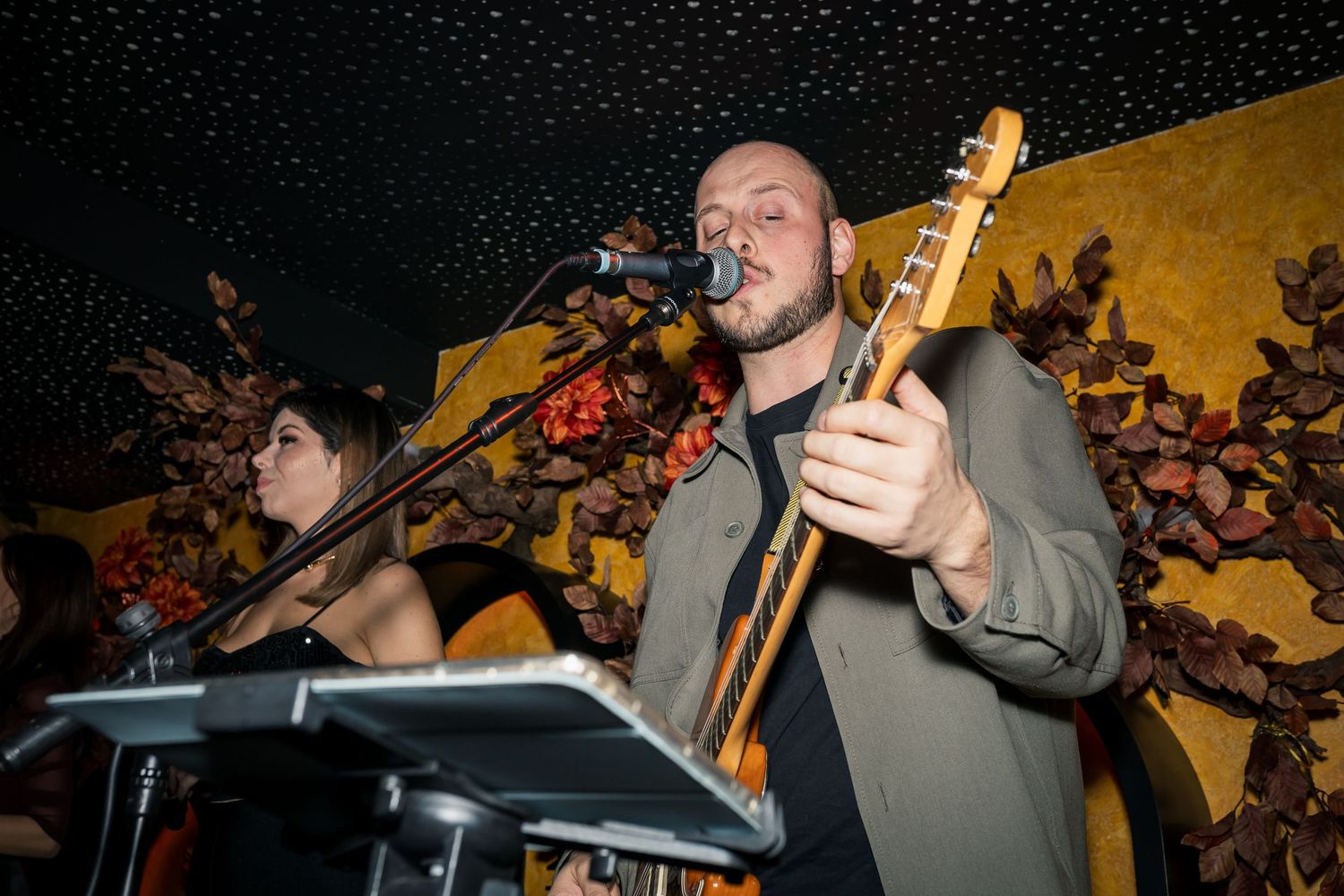 Male musician playing bass guitar and singing into microphone at live indoor venue event.