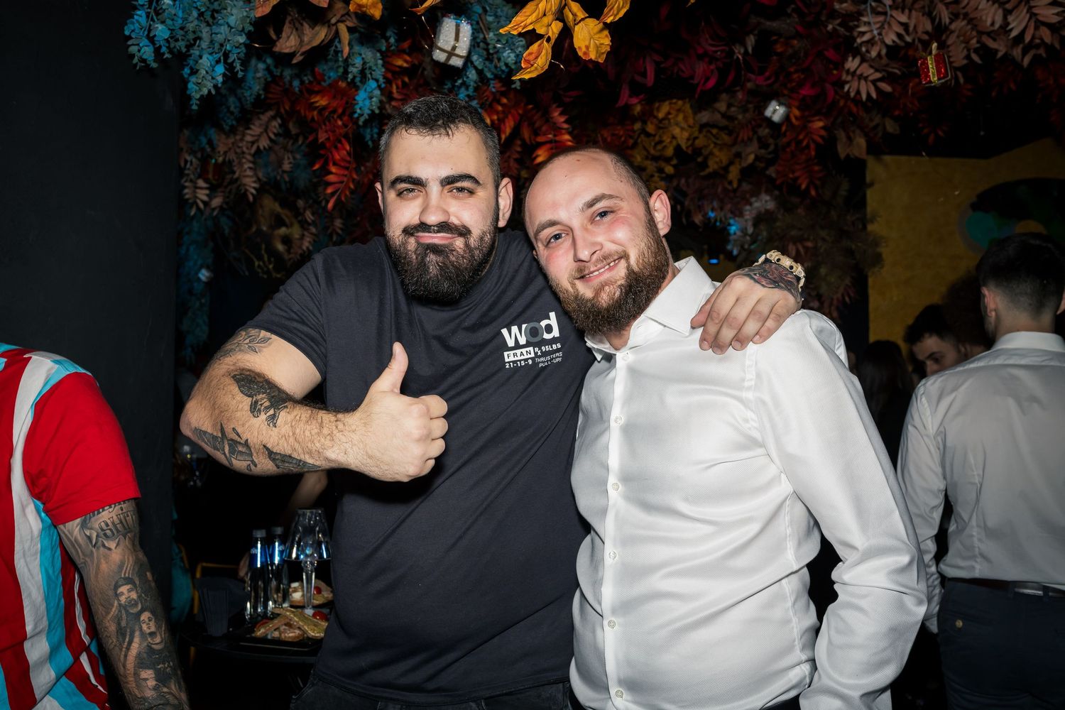 Two smiling men posing together at lively indoor party, one wearing a chef uniform.