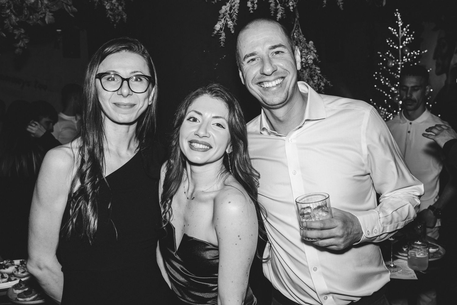 Three friends smile together at an elegant black and white party event.