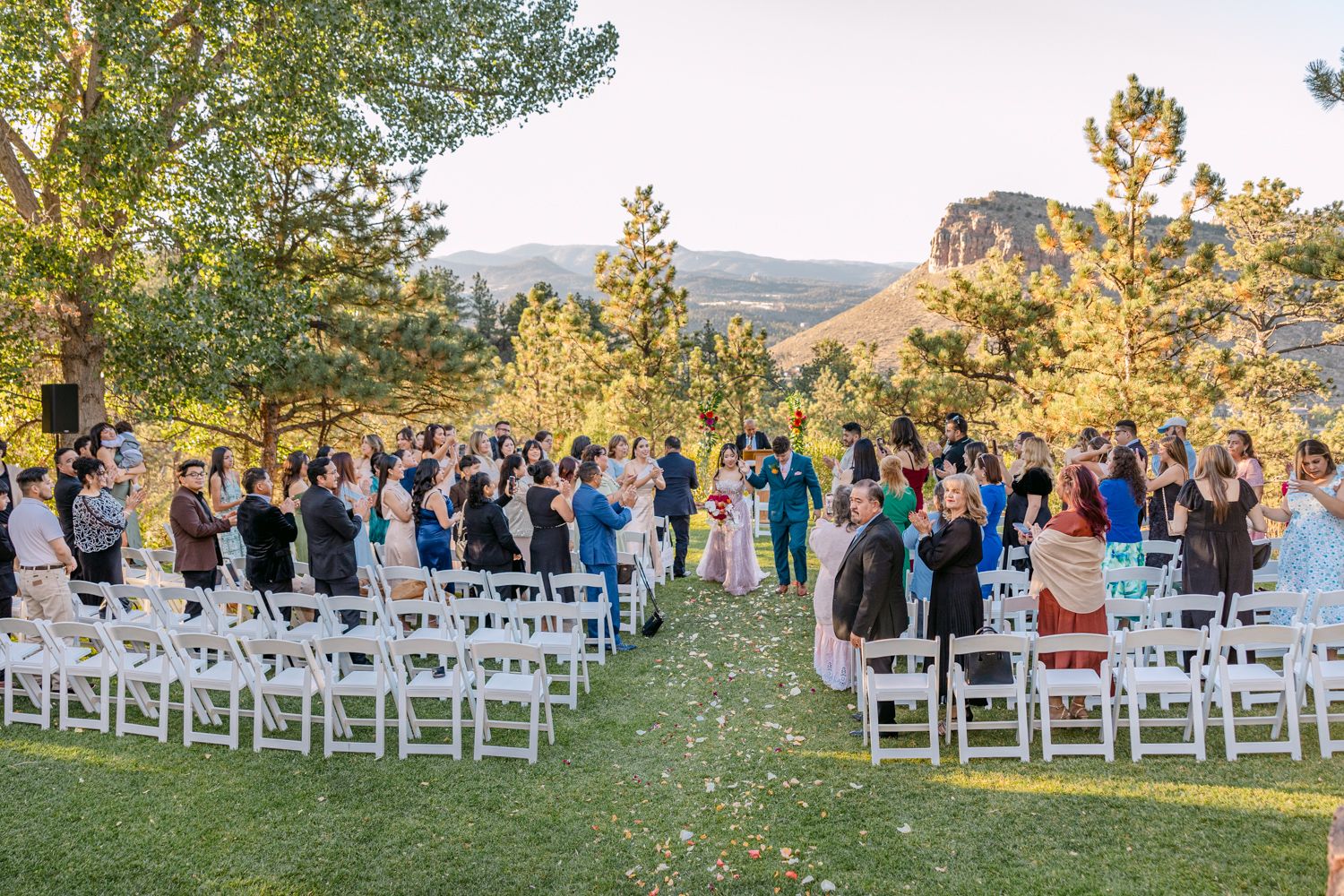 White wooden chairs arranged in rows for an outdoor wedding ceremony with mountains and pine trees in the background.