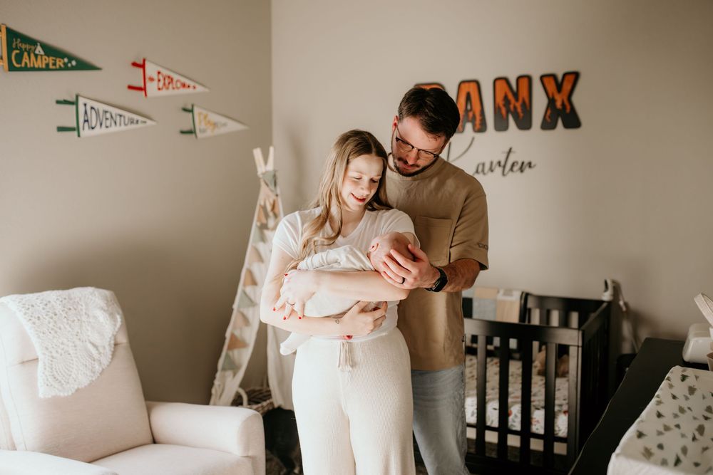 Parents holding newborn baby in nursery with decorative wall art and pennants.