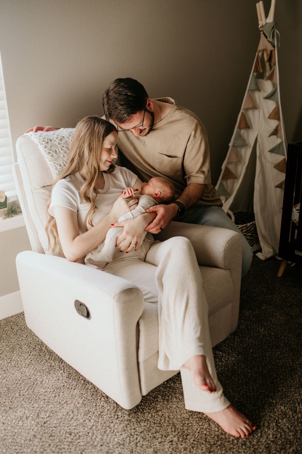 Couple with newborn baby relaxing in white recliner chair at home.