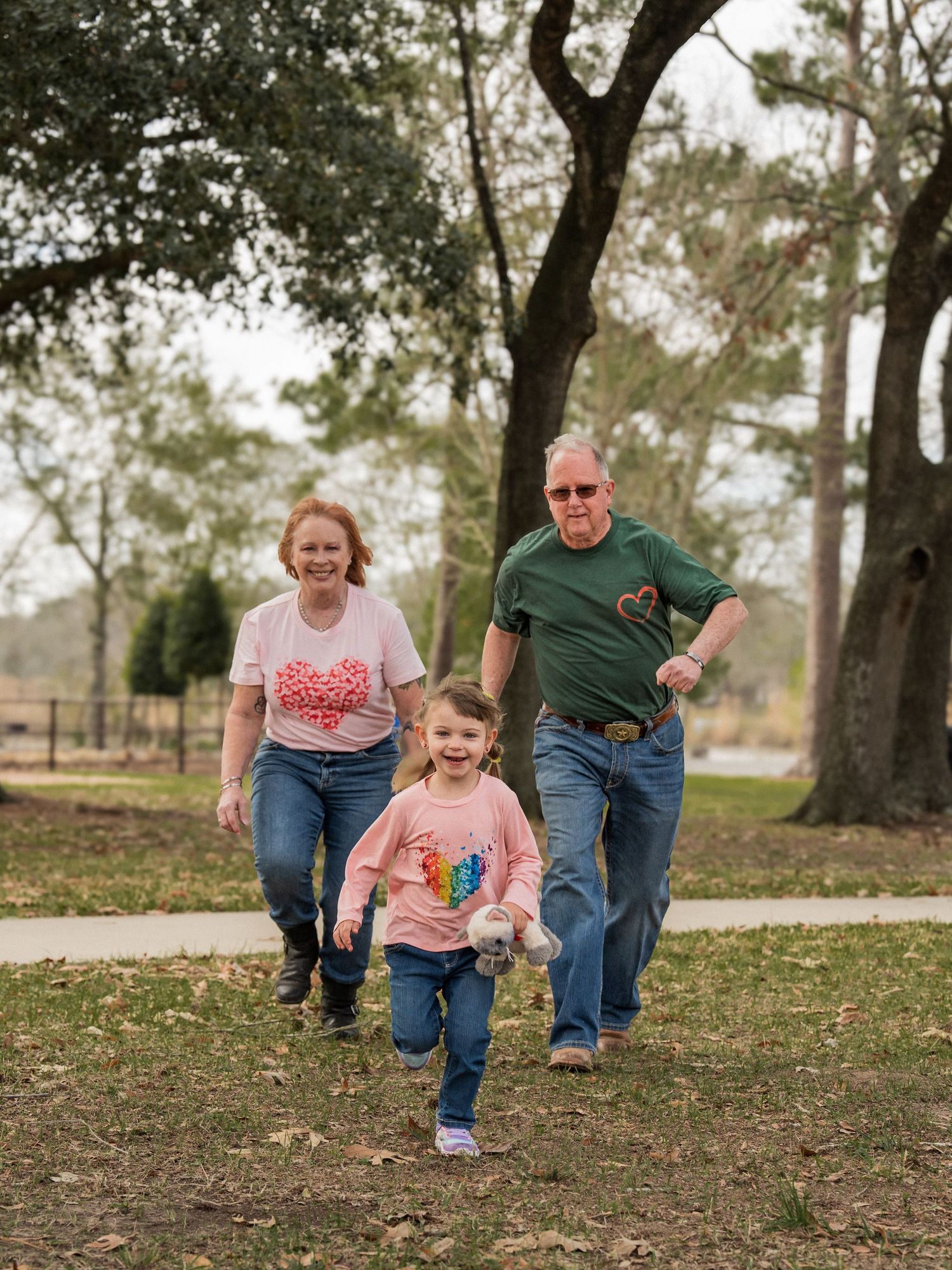 A family runs and plays together on fallen autumn leaves in a park setting during a lifestyle photo session.