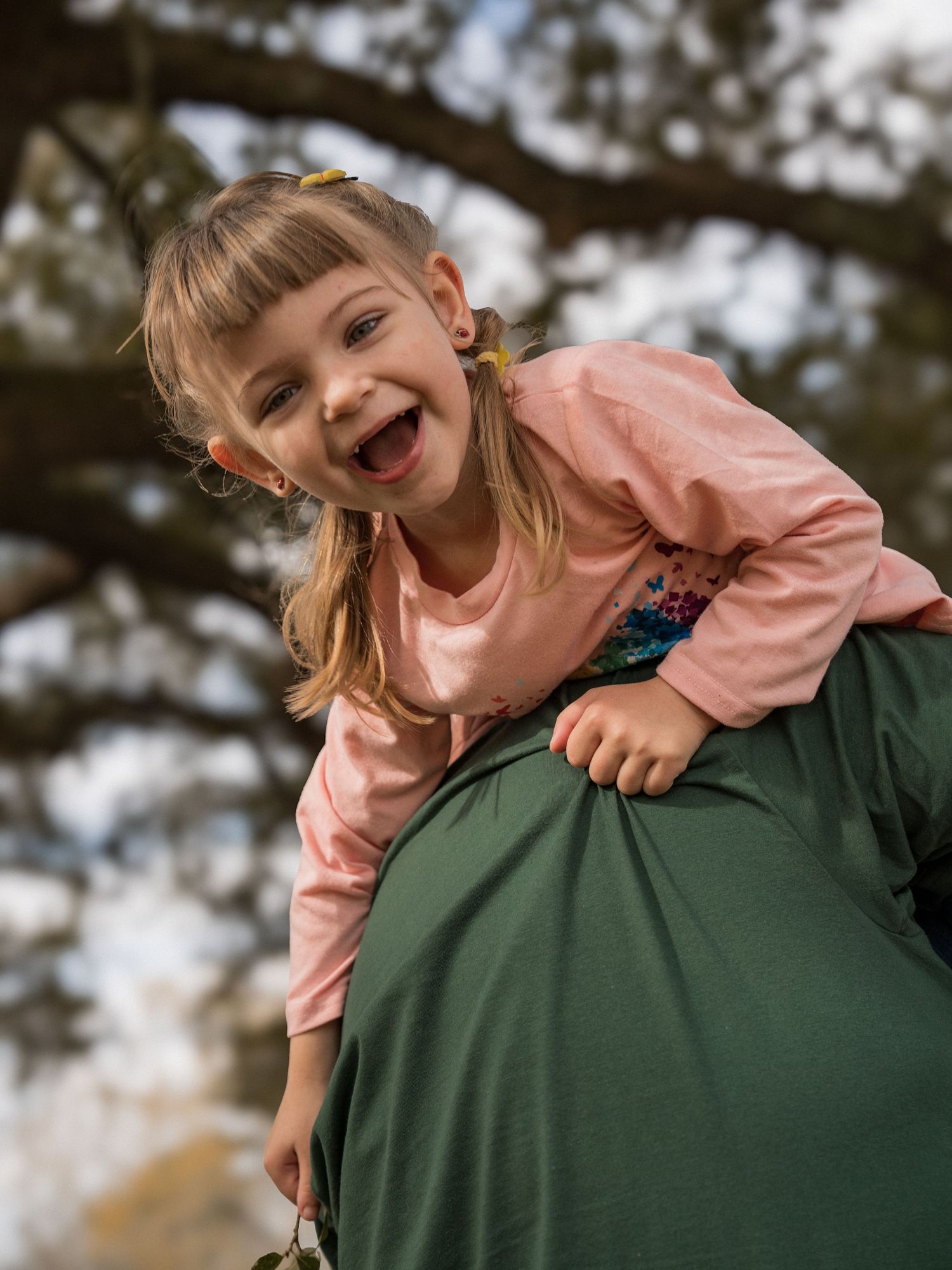 A joyful expression captured in a candid outdoor portrait wearing a pink sweater.