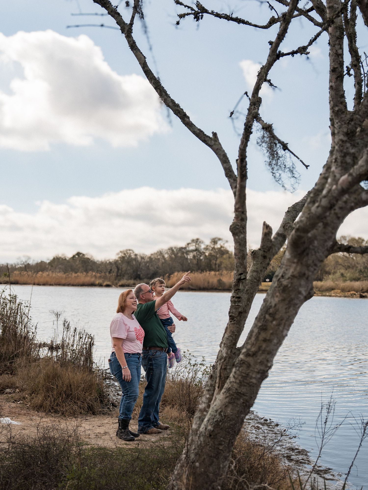 Family enjoys a peaceful afternoon fishing together by a serene lake with bare trees on a cloudy day.