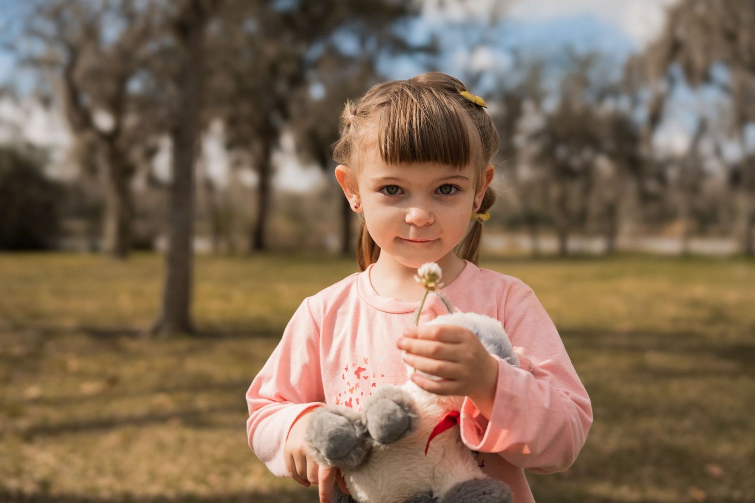 A sweet moment outdoors holding a small flower in a pink sweater against a natural background.