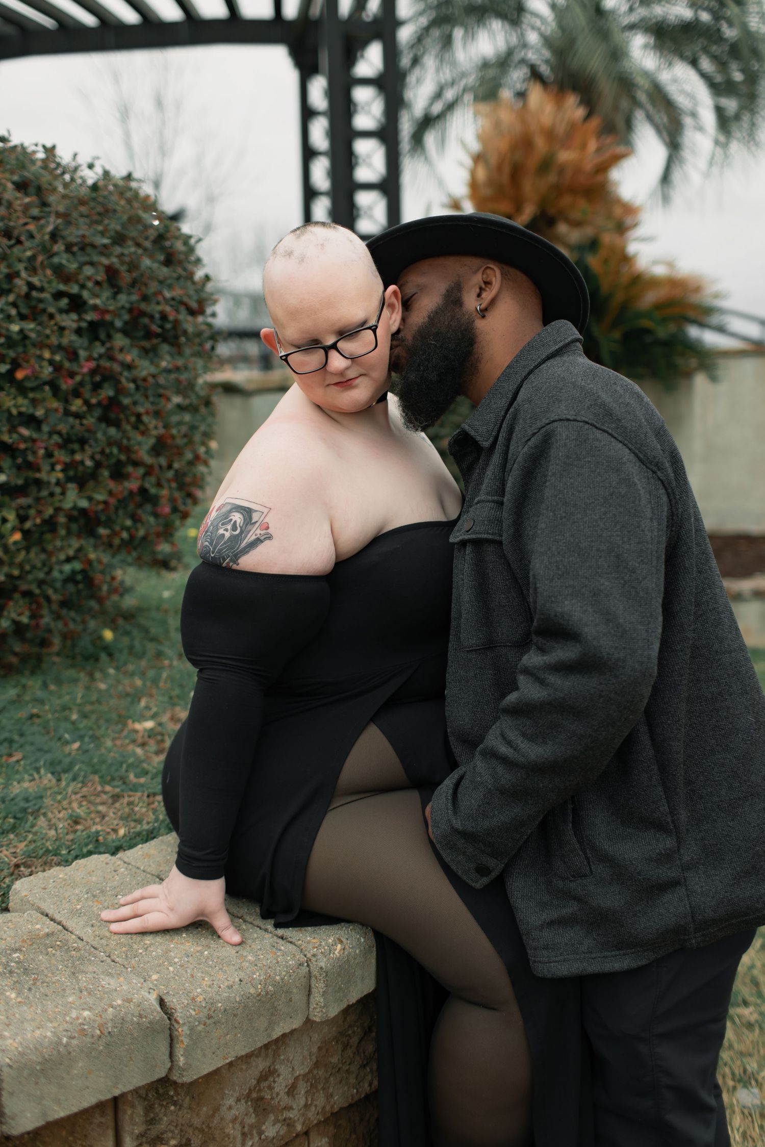 A romantic couple shares intimate moments together while sitting on a stone wall in an outdoor autumn setting.