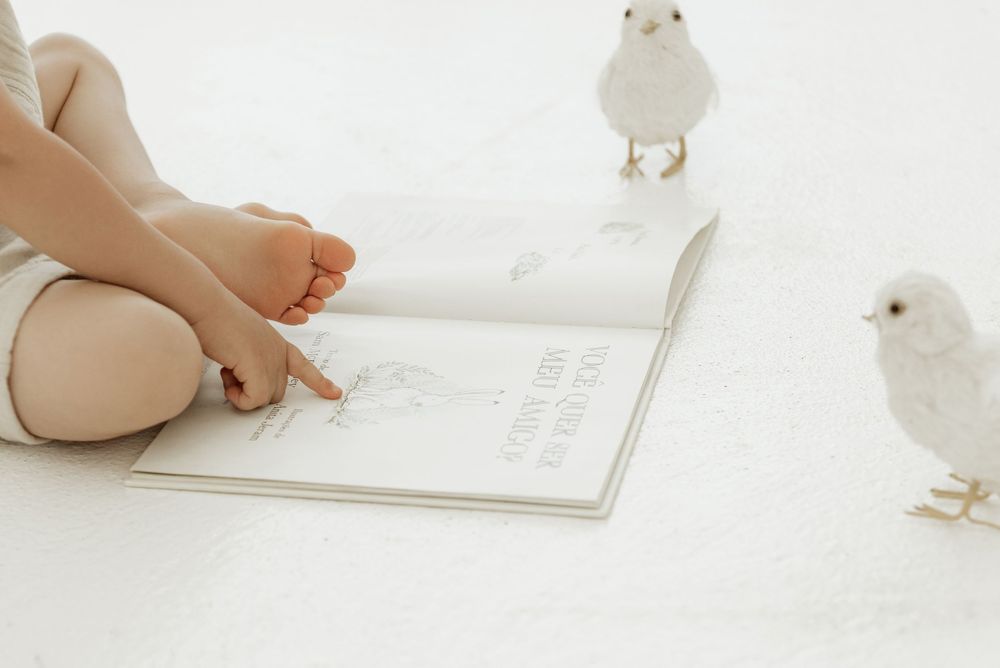 A small white chick stands near an open book on a white surface, creating a minimalist composition.