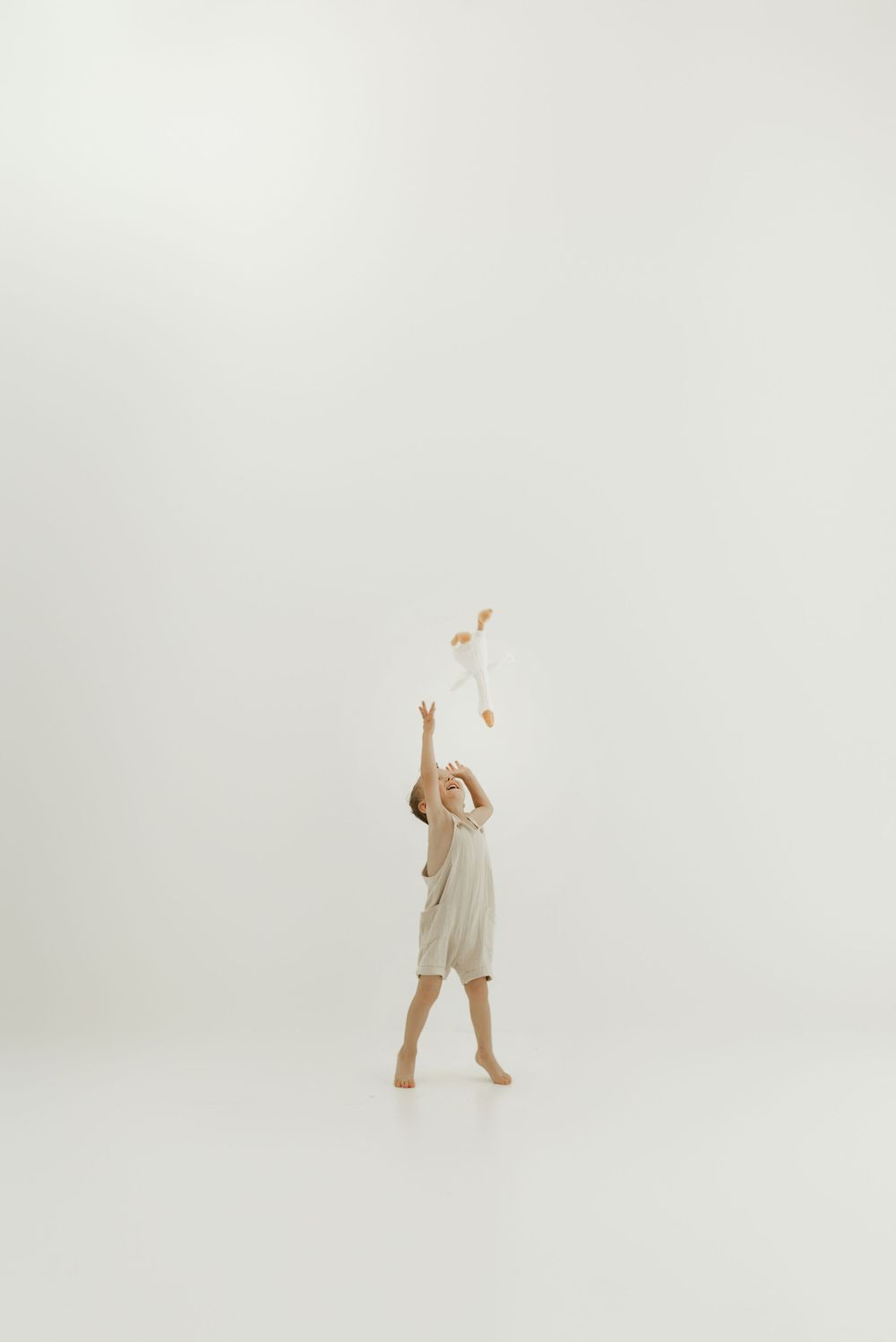 Child in white clothing jumps and dances joyfully against a bright minimalist background.