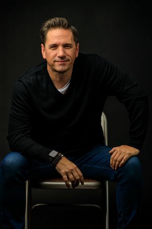 Professional studio portraits against dark background showing casual poses in black sweater and jeans. portrait photography st louis.