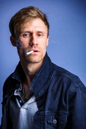 Portrait series against blue background wearing denim jacket and smoking. photography st louis.