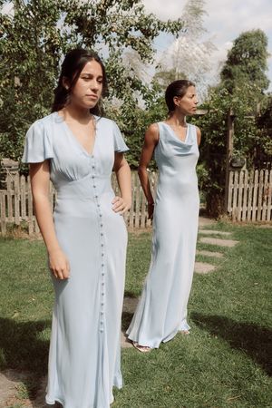 Light blue summer dresses shown from different angles on a sunny lawn with a picket fence in the background.