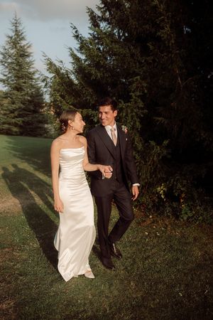 Bride and groom share playful moments walking together through an evergreen forest setting at Birtsmorten Court