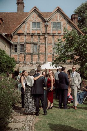 Elegant gathering outside historic Tudor-style brick building with timber framing and garden setting  at Birtsmorten Court