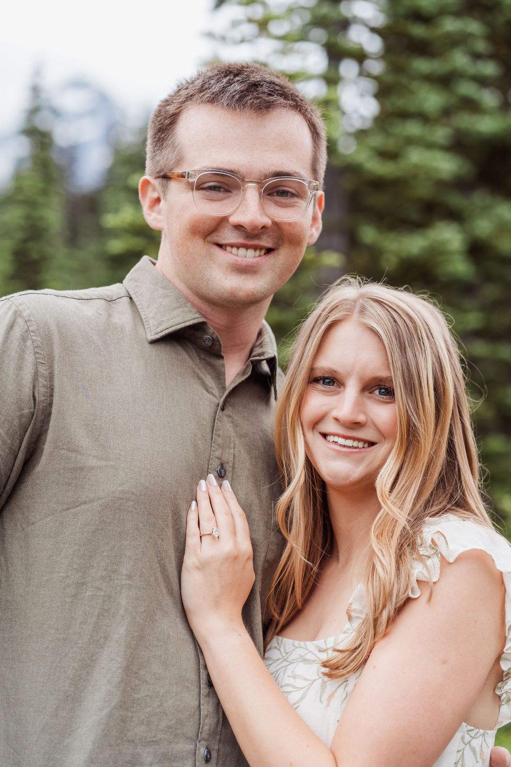 A couple in a romantic outdoor photoshoot with evergreen trees in the background.
