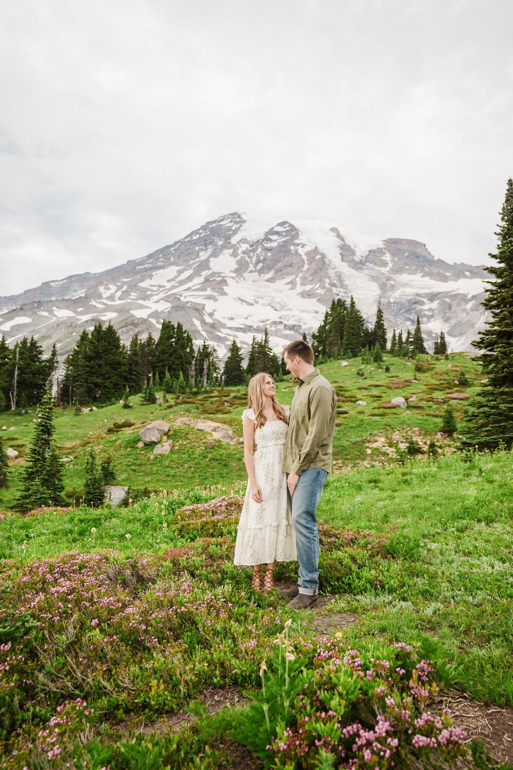 An Engaged couple stands in a wildflower meadow with Mount Rainier's snow-capped peak rising majestically in the background.