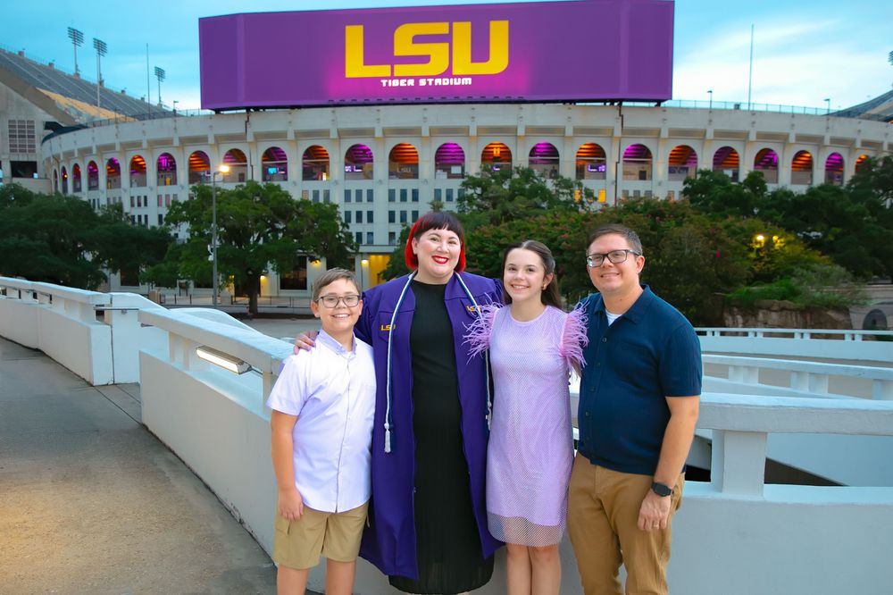 LSU graduate celebrating with family in front of the LSU marquee