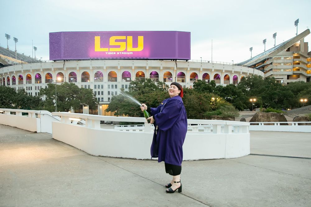LSU graduate popping champagne in front of LSU marquee