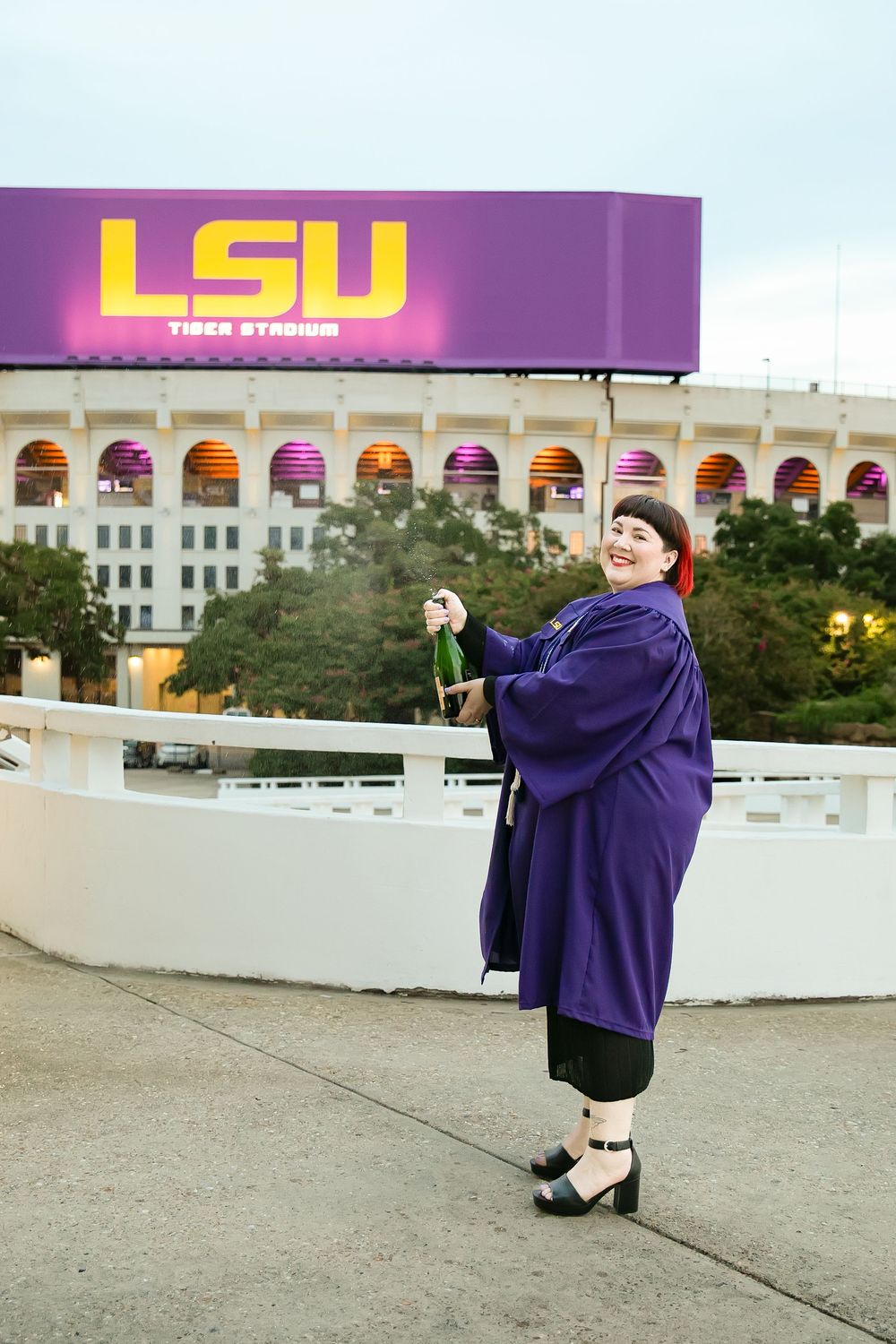 LSU graduate popping champagne in front of LSU marquee