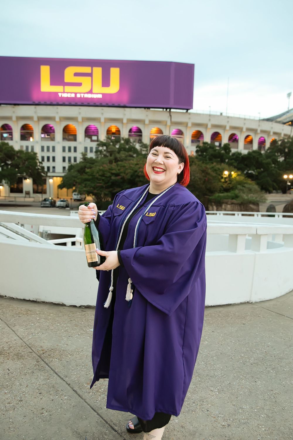 LSU graduate popping champagne in front of LSU marquee