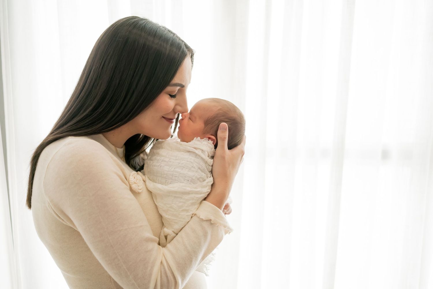 A collection of black and white family photos showing tender moments between parents and baby near a window.