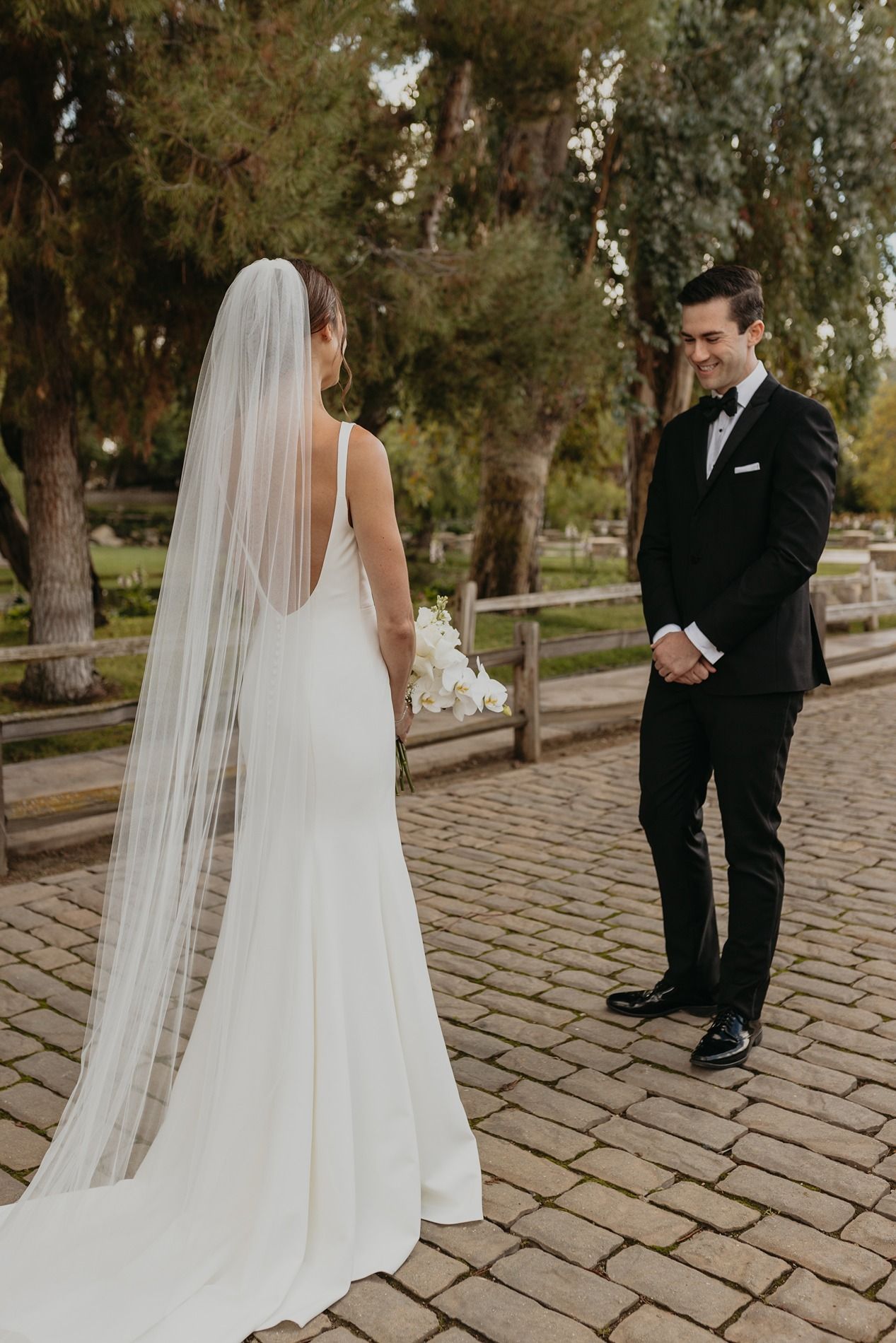Bride and groom share an intimate first look moment on stone pathway surrounded by trees at at Lake Oak Meadows in Temecula.