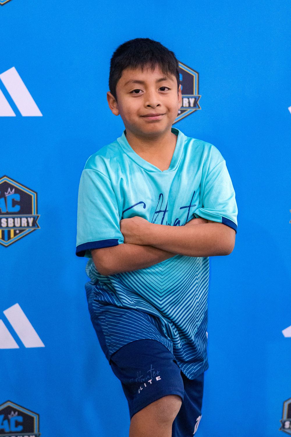 Soccer player in turquoise gradient jersey poses confidently against blue backdrop with sports logos.
