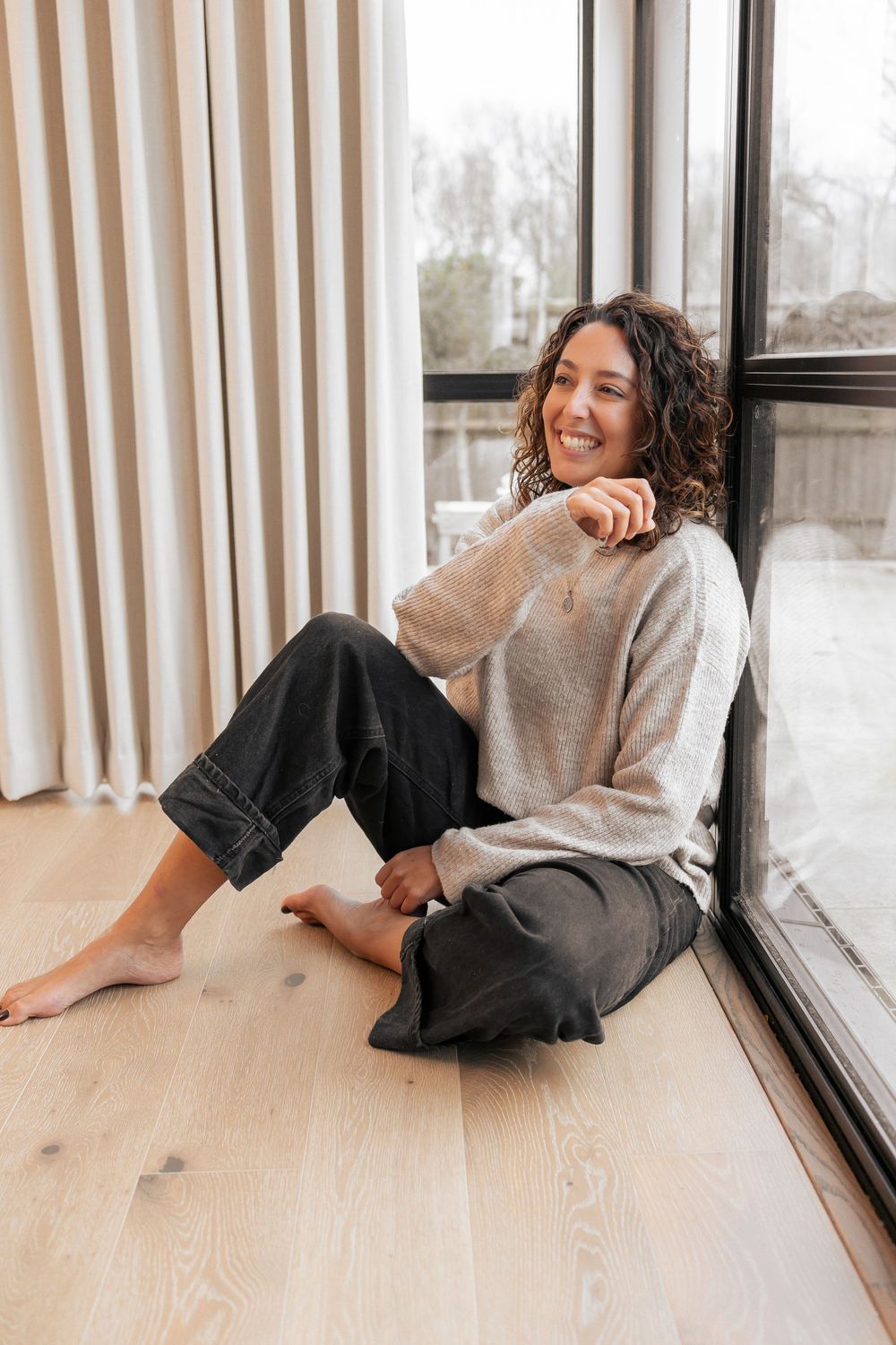 Person relaxing by window wearing cozy sweater and dark pants on wooden floor. Photography in Buckinghamshire.
