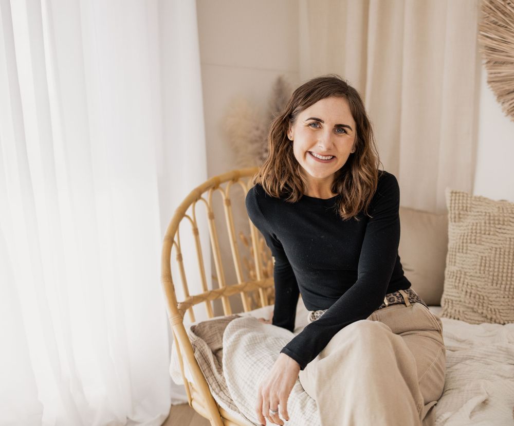 A person in a black sweater sits comfortably on a wooden chair near white curtains and neutral decor.Photography in Buckinghamshire.