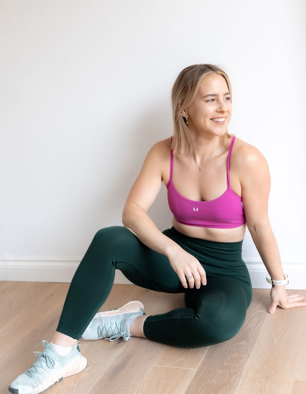 A person in a pink sports bra and black leggings performs stretching exercises on a wooden floor. Photography in Buckinghamshire.