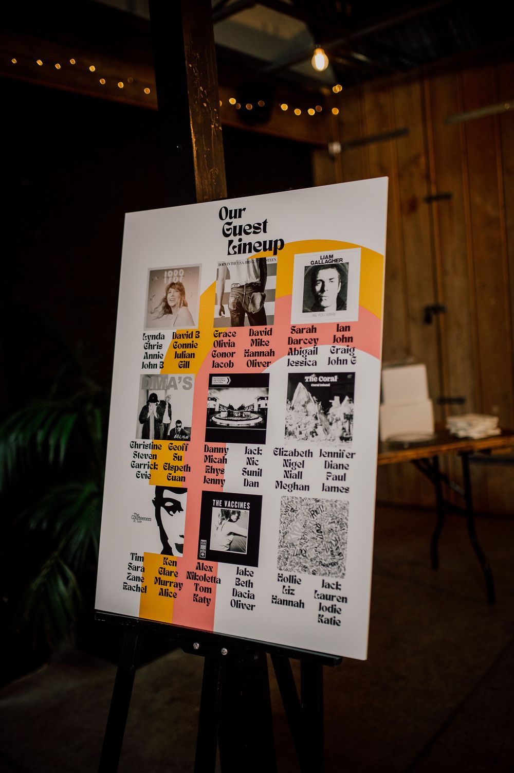 A wedding seating chart display board on an easel with colorful blocks showing guest groupings and photos in a rustic venue.