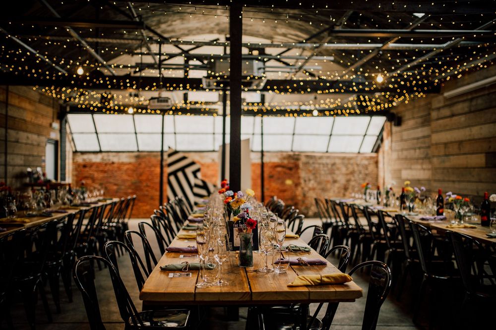 Rustic wedding reception venue with wooden walls, string lights, and long tables set for dinner service.