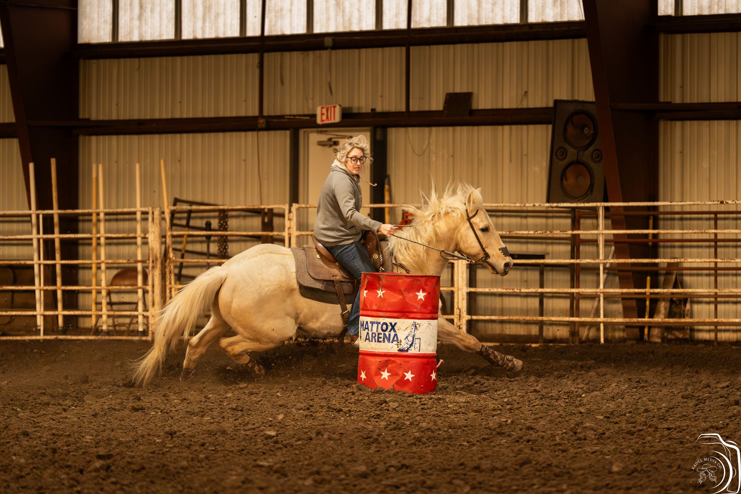 Barrel racer riding palomino horse around competition barrel in indoor equestrian arena.