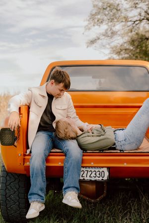 Couple relaxing on the tailgate of a vintage orange truck in a scenic outdoor setting.