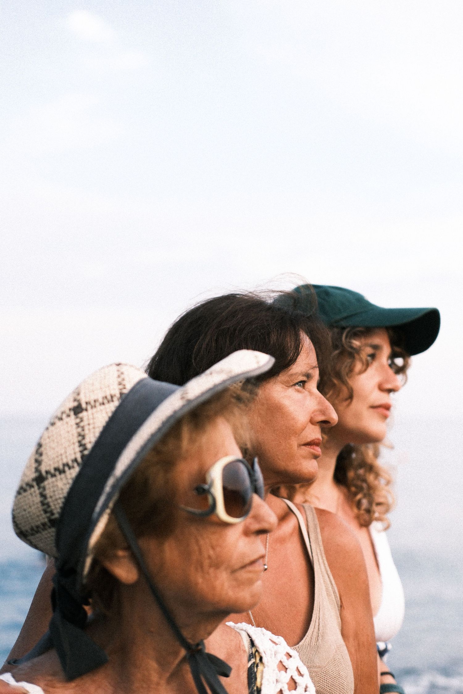 Group of friends wearing hats and sunglasses looking out at ocean view on sunny day.