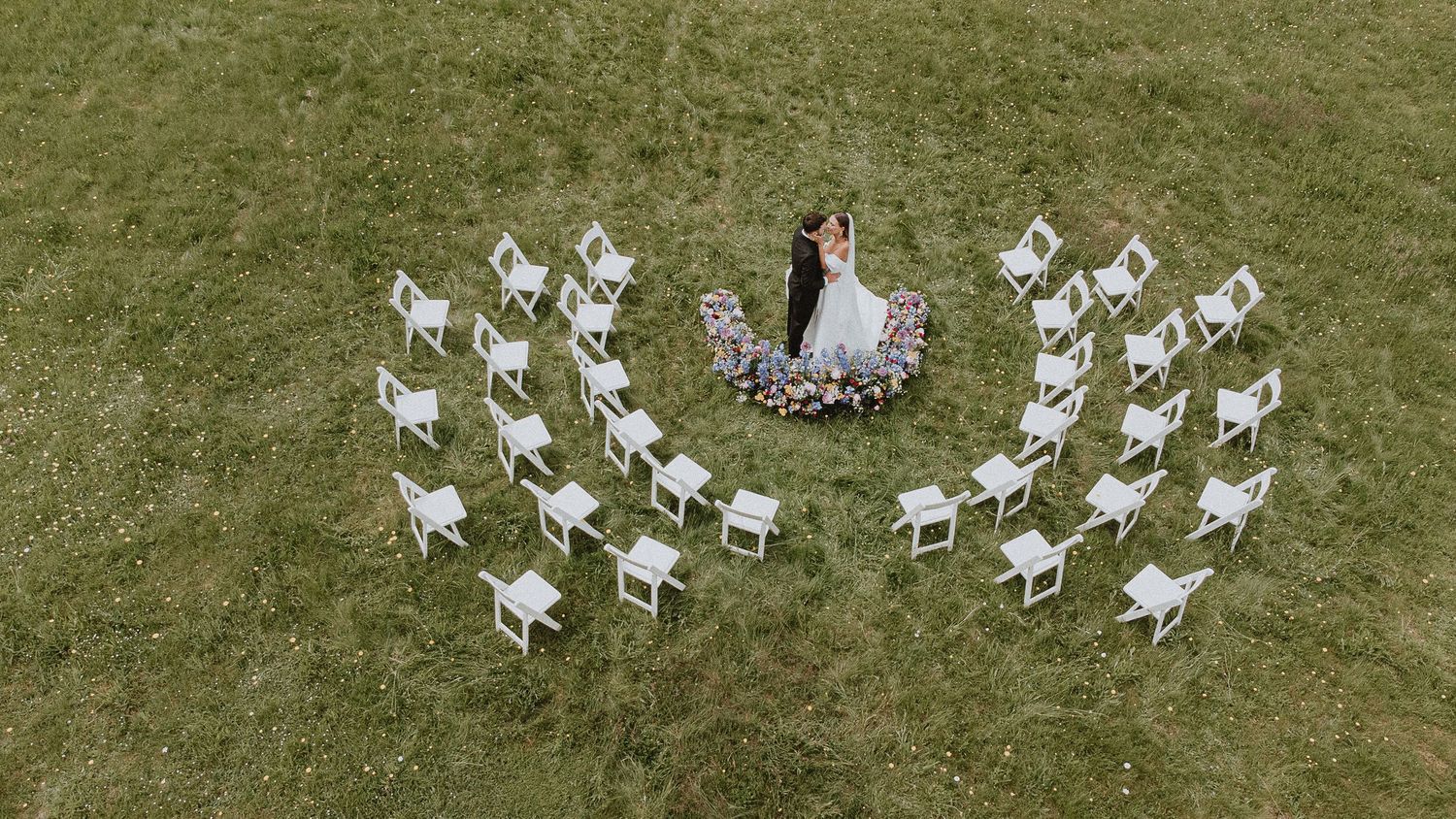 French wedding captured by a French photographer: couple kissing at a scenic château in France, surrounded by white chairs and wildflowers —