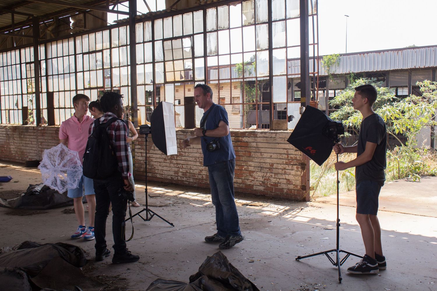 GETPIX photography instructor demonstrating studio lighting setup to students with models in a gritty factory environment.
