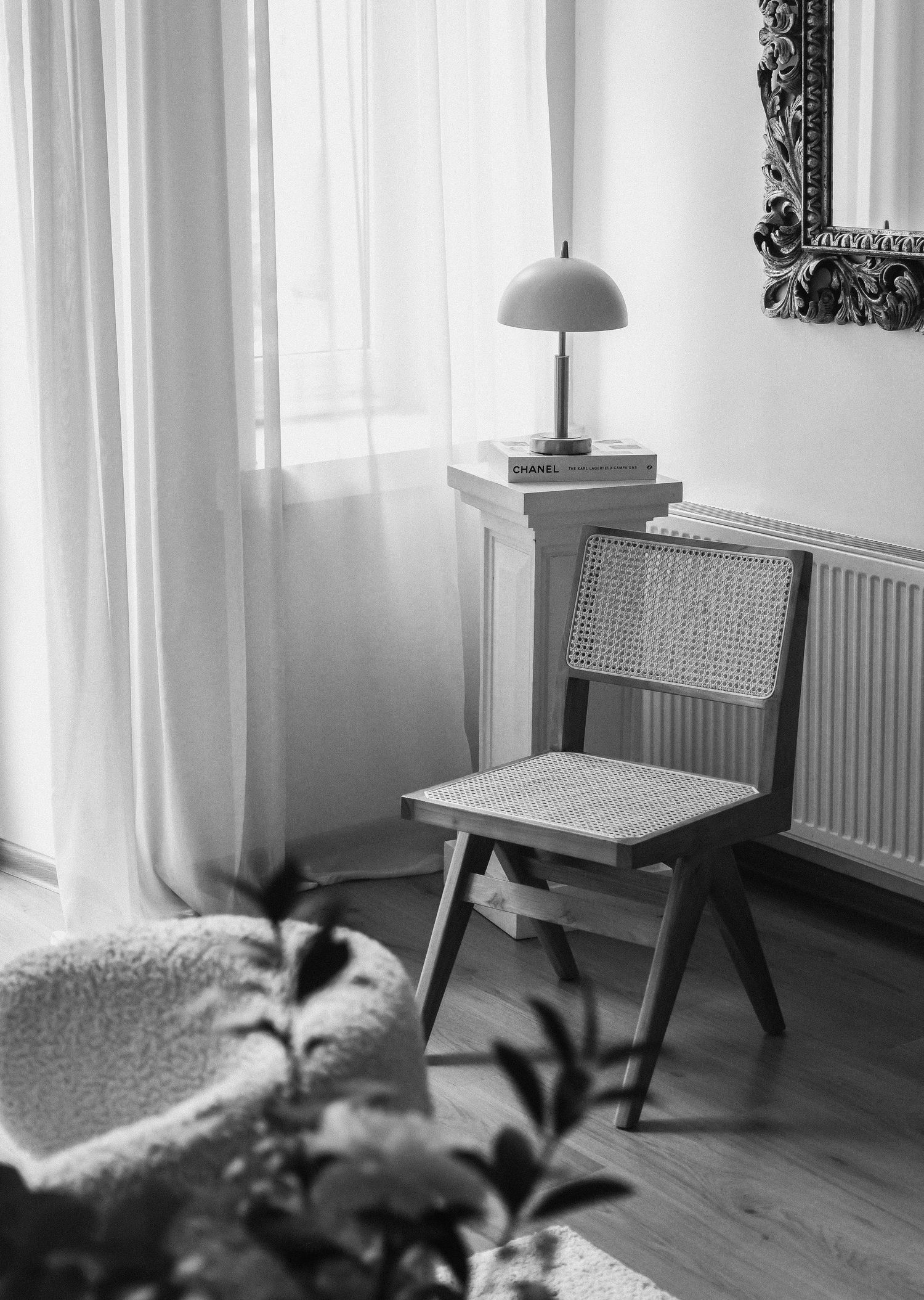 Black and white interior photo of a minimalist living room with white curtains, radiators, and modern furniture.