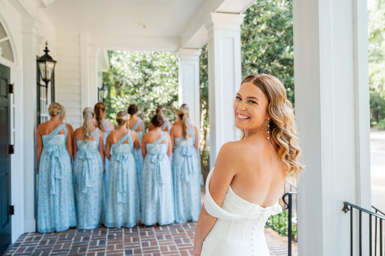 Wedding party on white columned porch with bridesmaids in light blue dresses.