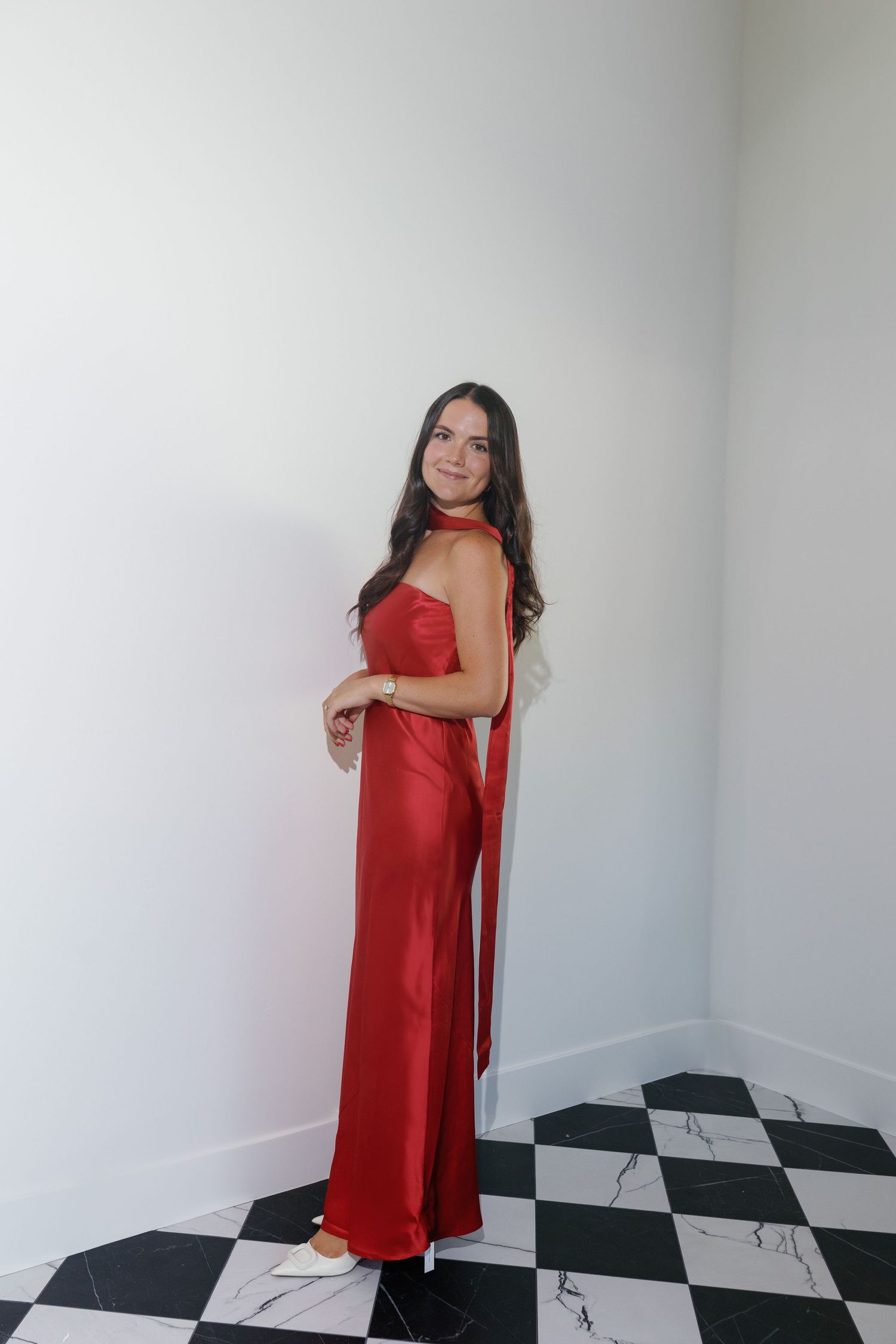 Woman in a flowing red gown poses on a black and white checkered floor.