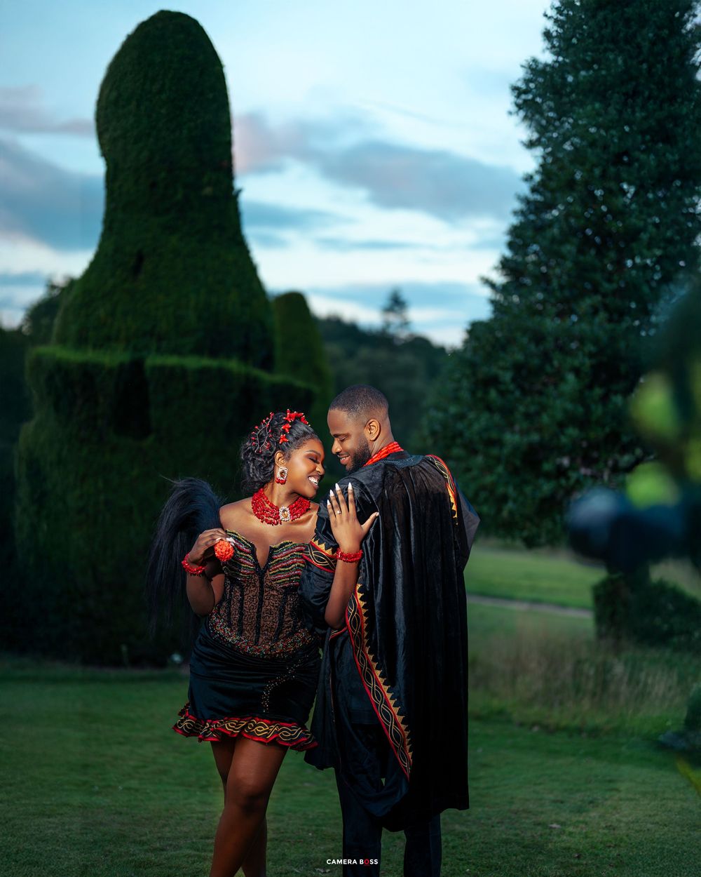 A couple embraces in a romantic outdoor photoshoot against a moody evening sky and green landscape.
